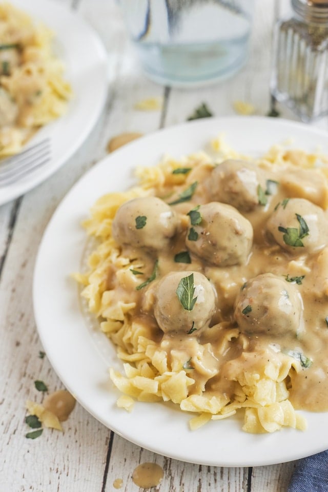 Close up photo of swedish meatballs over egg noodles on a white plate on kitchen table