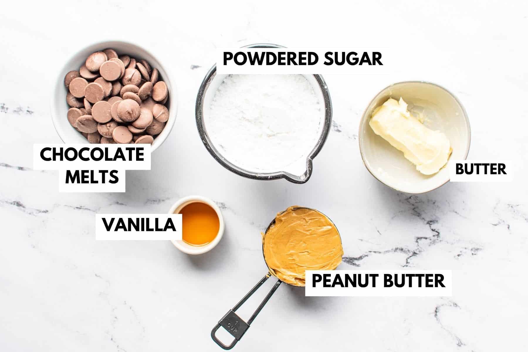 Five labeled ingredients are arranged on a white surface—just what you’ll need for this classic peanut butter balls recipe: chocolate melts in a bowl, powdered sugar in a sifter, a dish of butter, vanilla in a small bowl, and peanut butter in a measuring cup.