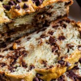 Two slices of avocado banana bread in front of the whole loaf with recipe title on top of image