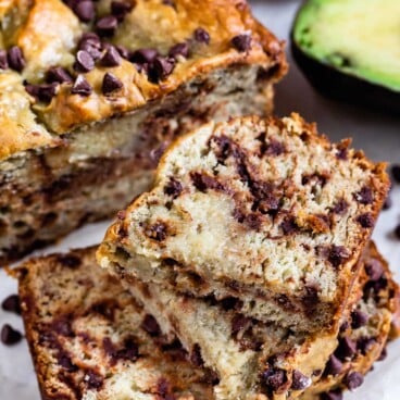 Avocado banana bread loaf cut into slices and stacked in front of the rest of the loaf