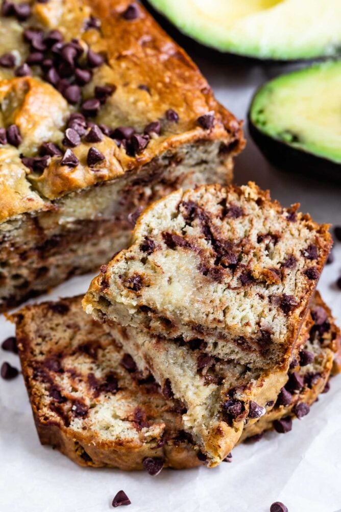 Avocado banana bread loaf cut into slices and stacked in front of the rest of the loaf