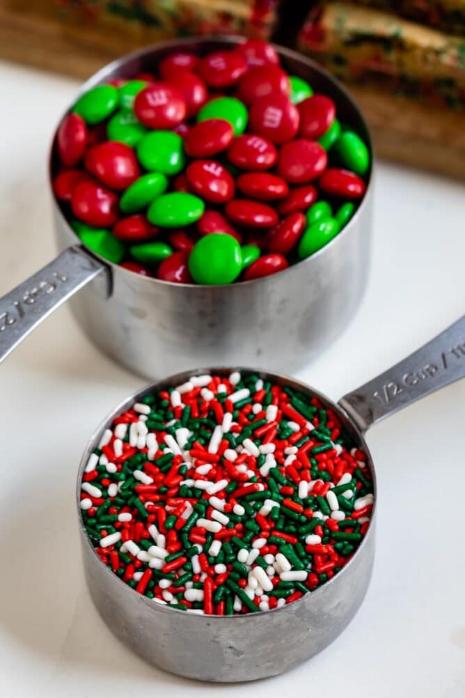 Overhead view of m&m's and sprinkles in two stainless steel measuring cups