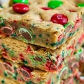 Stack of christmas cookie bars with m&ms around them and recipe title on top of image