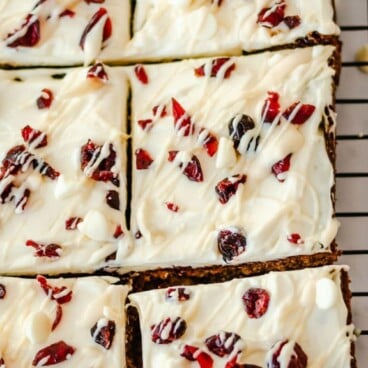 Overhead view of cranberry bliss bars on a metal cooling rack cut into squares with recipe title on top of photo