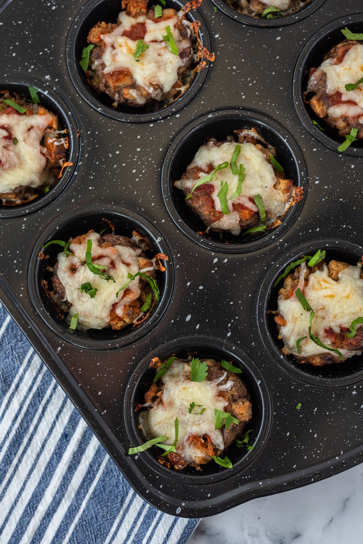 Overhead shot of baked mini meatloaves covered in cheese still in muffin tins