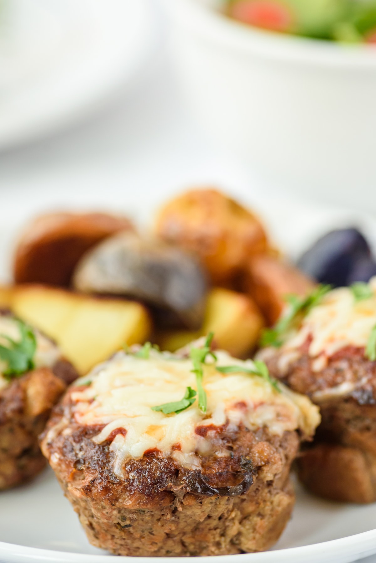 Side shot of mini meatloaves on a plate with veggies on the side