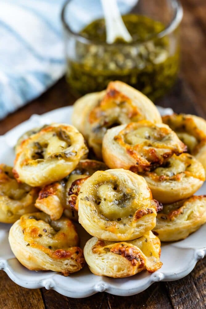 Pesto pinwheels on a white scalloped plate with pesto in background