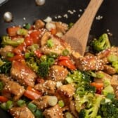 Chicken teriyaki being cooked in a wok with a wooden spoon