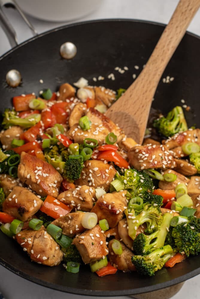 Chicken teriyaki being cooked in a wok with a wooden spoon