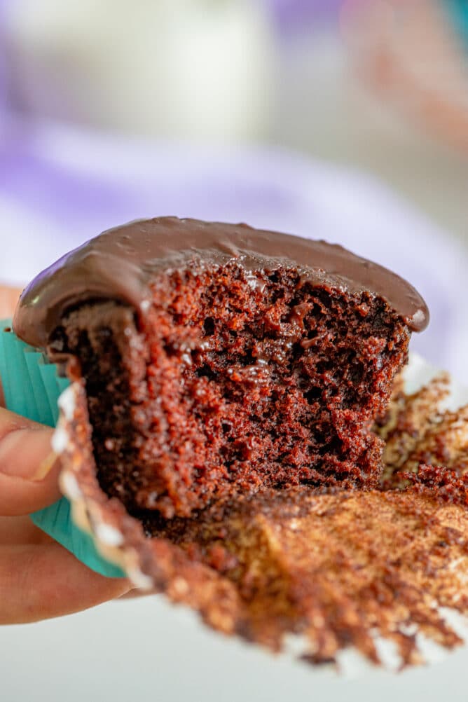 Chocolate cupcake being held in hand that's half eaten to show inside