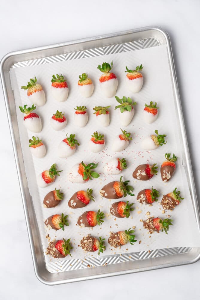 Overhead shot of sheet pan filled with white and milk chocolate covered strawberries some with toppings and some without