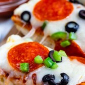 slices of French bread pizza with pepperoni and olives on cutting board