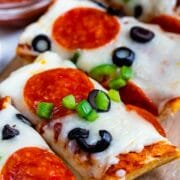 slices of French bread pizza with pepperoni and olives on cutting board