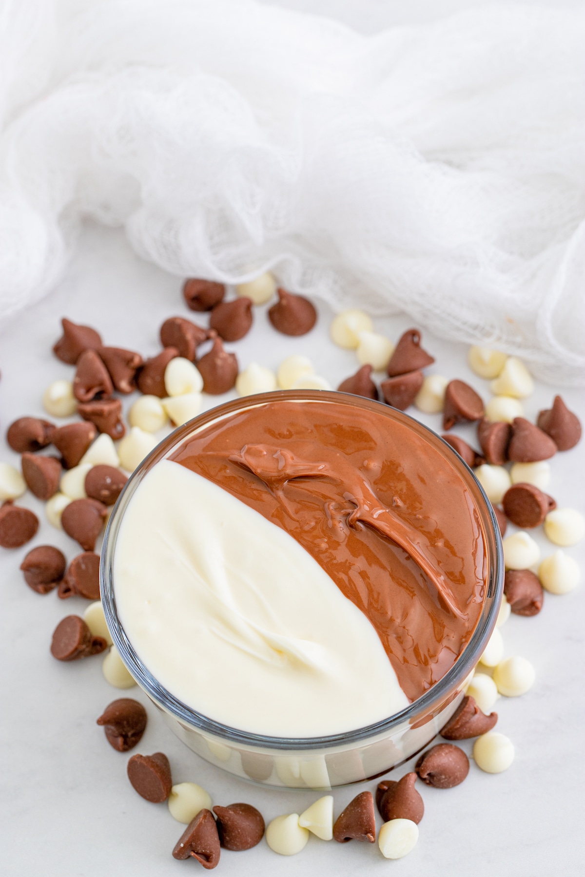 Bowl filled with half melted white chocolate and half melted milk chocolate with chocolate and white chocolate chips around it