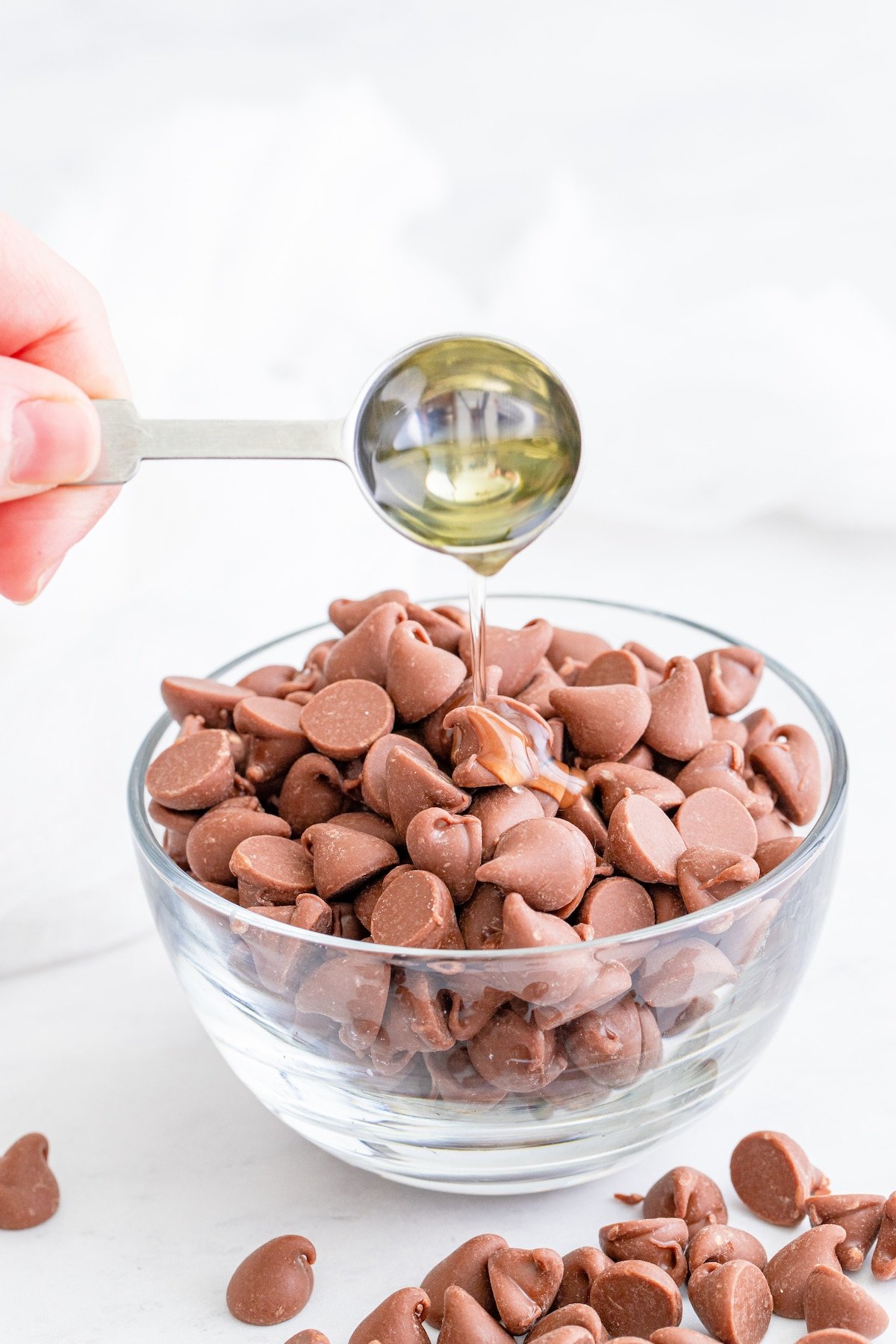 Teaspoon of oil being poured into a bowl of milk chocolate chips