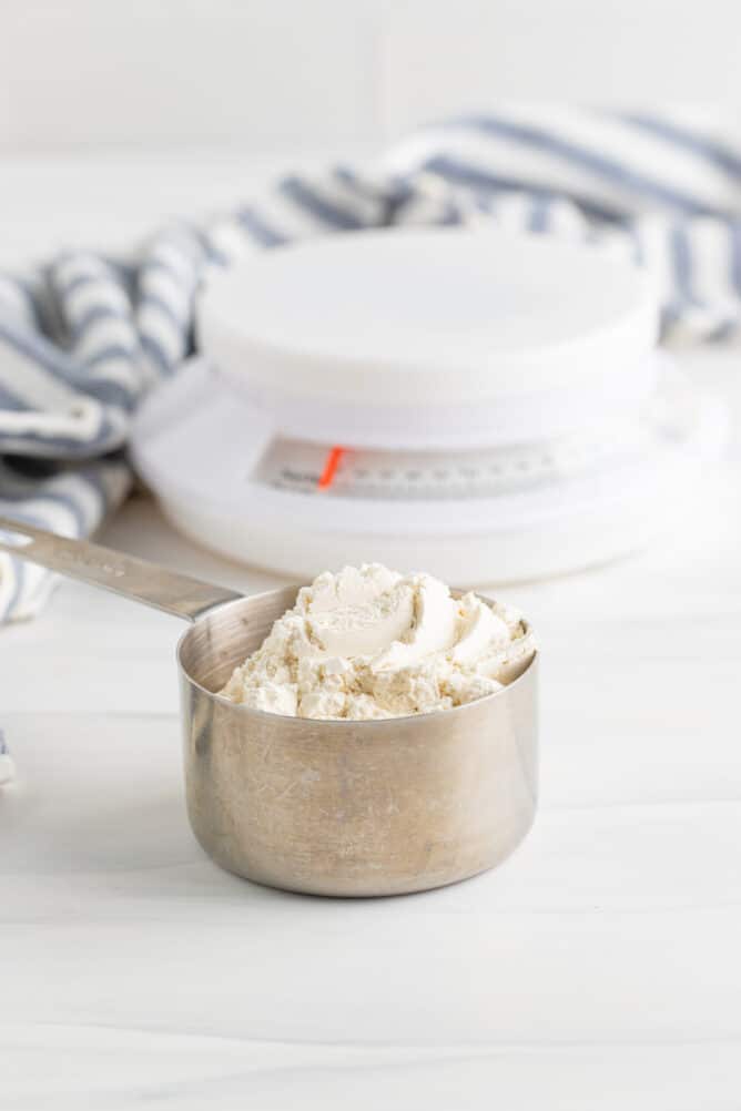 Measuring cup full of flour with kitchen scale in background