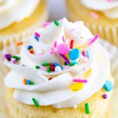 Close up of perfect vanilla cupcake with vanilla buttercream and topped with rainbow sprinkles and recipe title on top of image