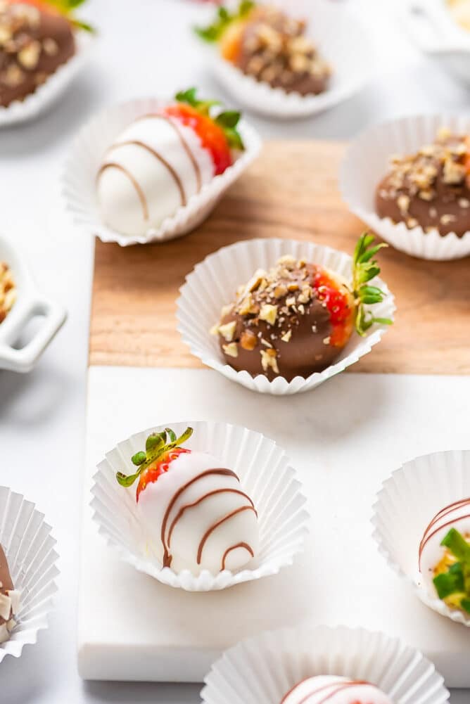 White and milk chocolate covered strawberries with different toppings in cupcake liners on a wood cutting board