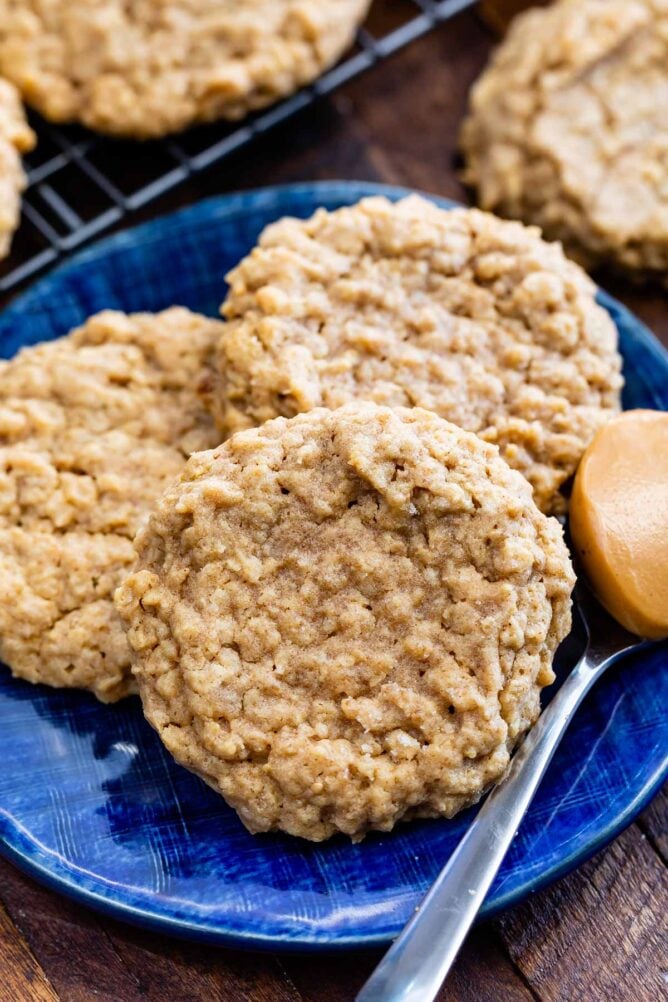 Three peanut butter oatmeal cookies on a royal blue plate next to a spoonful of peanut butter