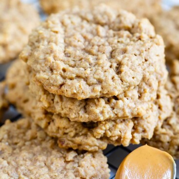 Peanut butter oatmeal cookies stacked on top of eachother on wire cooling rack next to a spoonful of peanut butter