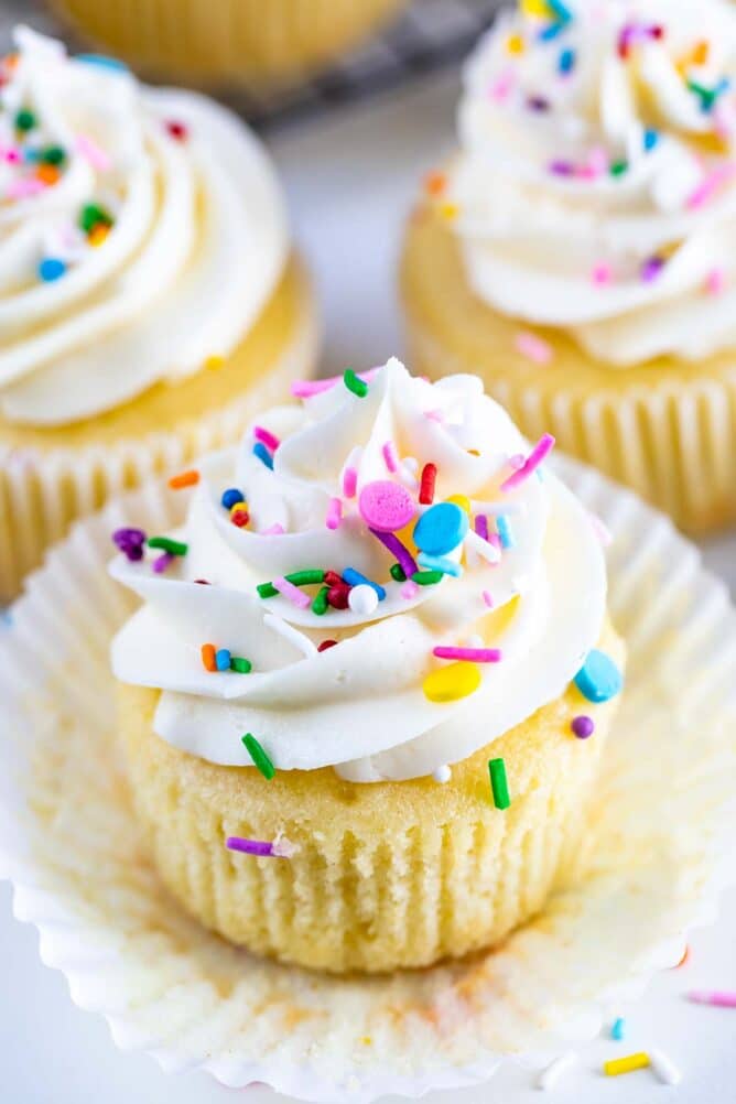Close up of perfect vanilla cupcake with vanilla buttercream and topped with rainbow sprinkles