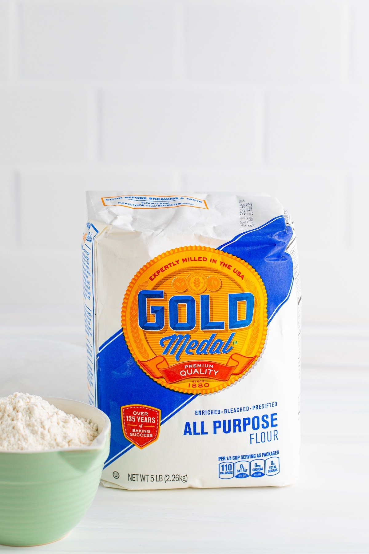 All purpose flour in the bag sitting next to a bowl full of flour