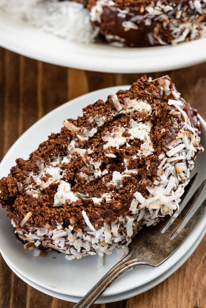 Slice of chocolate coconut cake roll on a white plate with fork