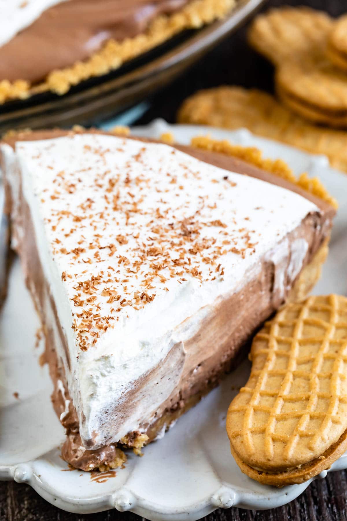 Close up of one slice of chocolate cream pie on a plate next to a peanut butter cookie