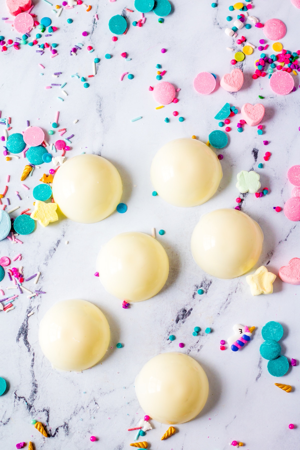 Overhead shot showing white hot chocolate bombs with unicorn sprinkles all around them