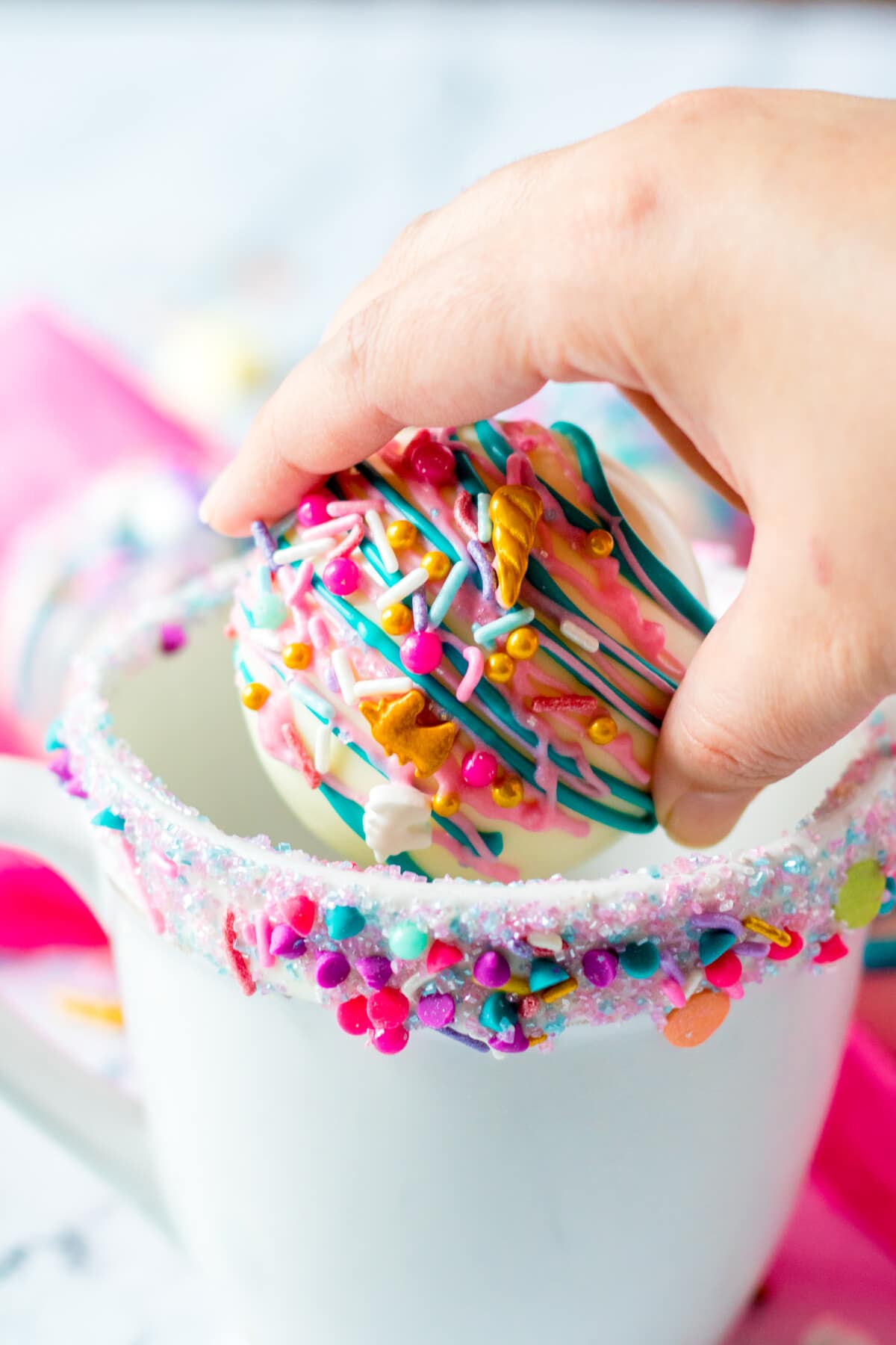 Hand placing one white hot chocolate bomb inside a mug