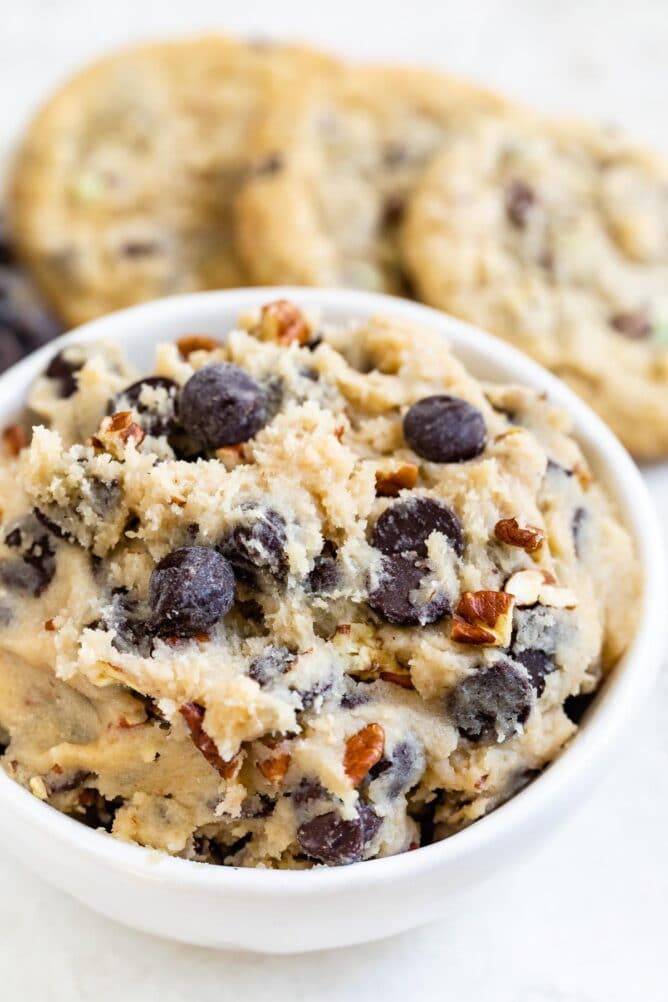 Close up shot of edible cookie dough with baked cookies in background