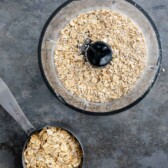 Overhead shot of old fashioned oats in a food processor after being processed and cup of old fashioned oats next to it