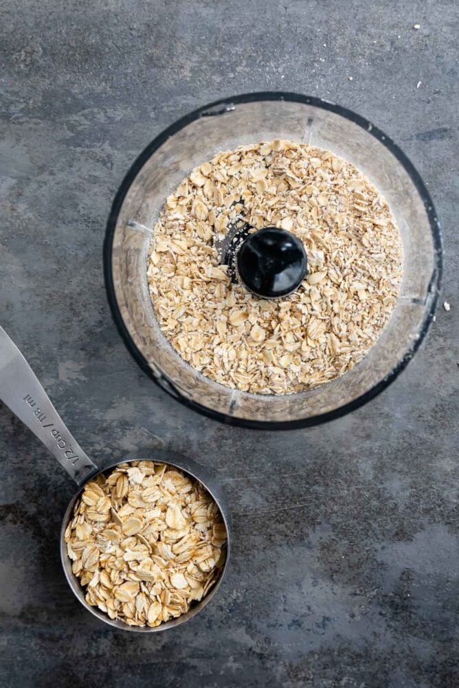 Overhead shot of old fashioned oats in a food processor after being processed and cup of old fashioned oats next to it