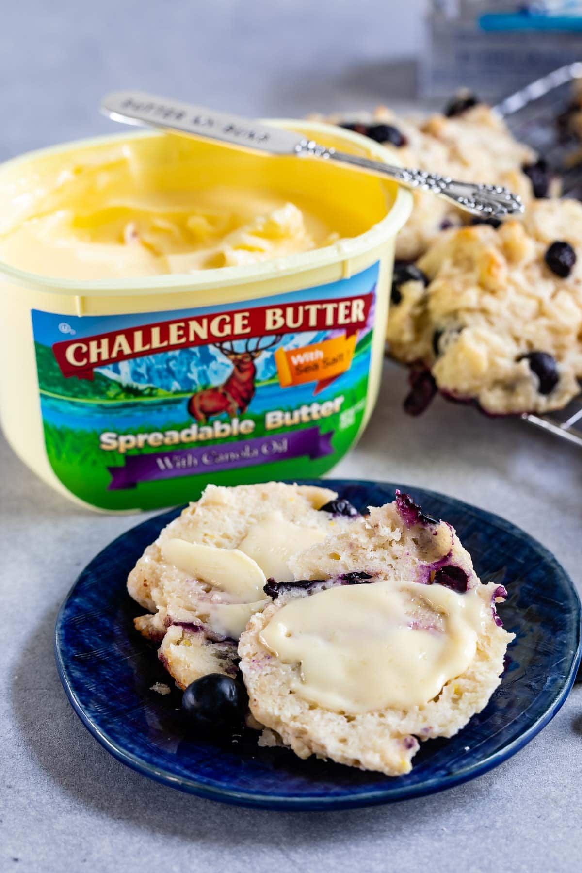 sliced biscuit on blue plate with butter on it and Challenge spreadable butter tub behind