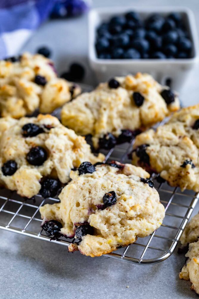 close up of blueberry biscuit on rack with blueberries behind