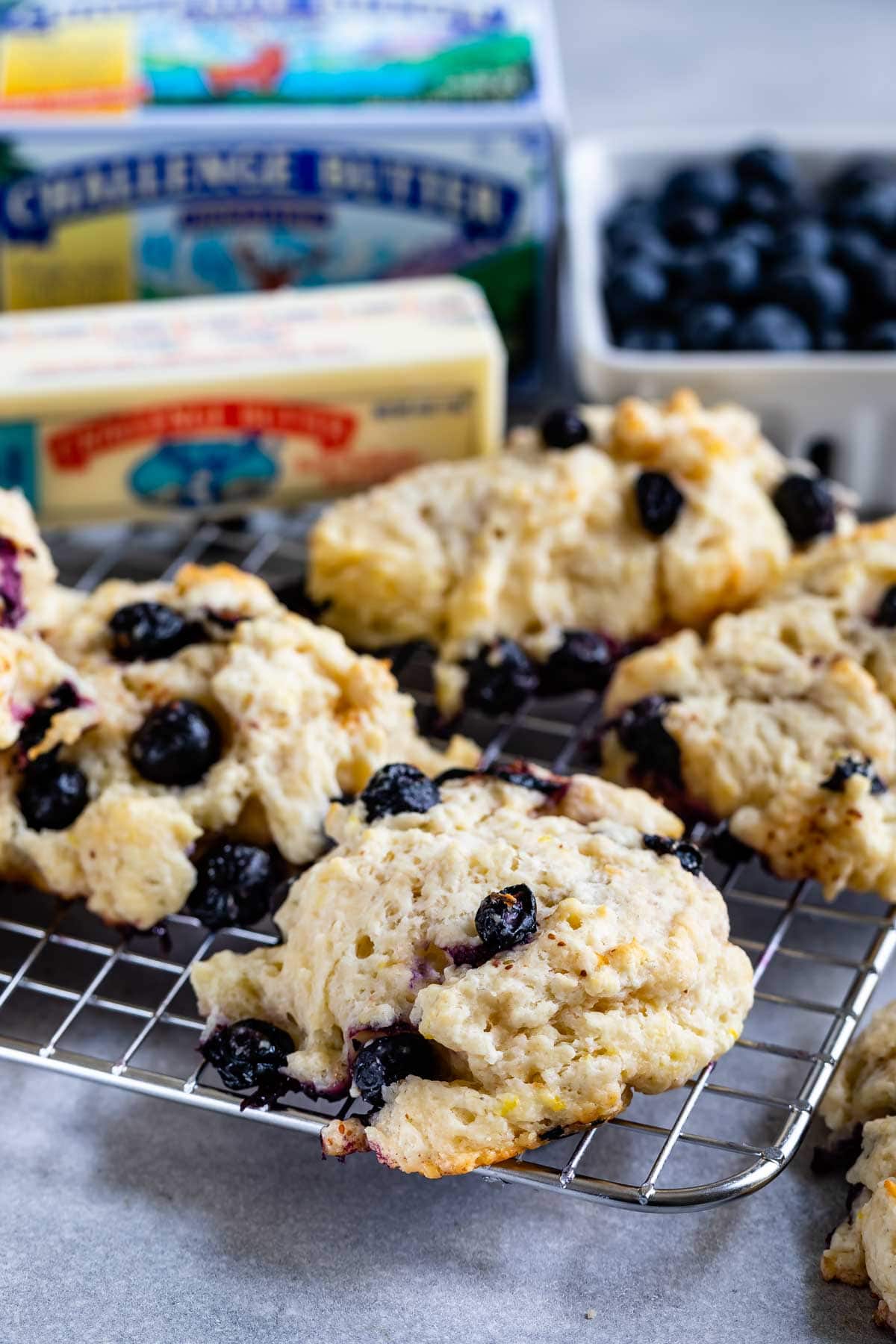 close up of blueberry biscuit on rack with blueberries and Challenge butter behind