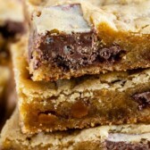 Stack of caramel crunch blondies with crunch candy bars next to it and recipe title on bottom of image