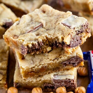 Stack of caramel crunch blondies with top blondie missing a bite and crunch candy bars next to it