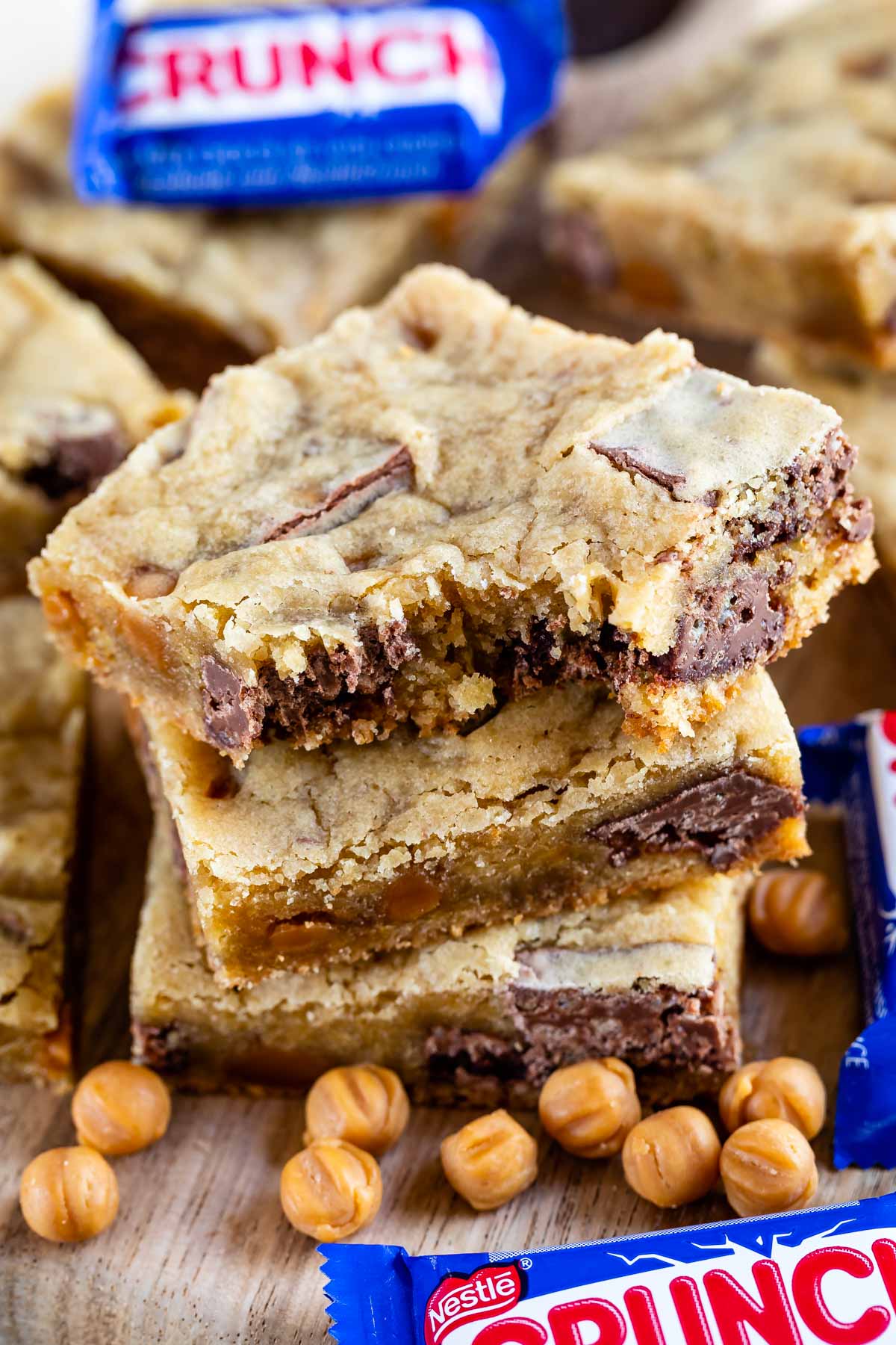 Stack of caramel crunch blondies with top blondie missing a bite and crunch candy bars next to it