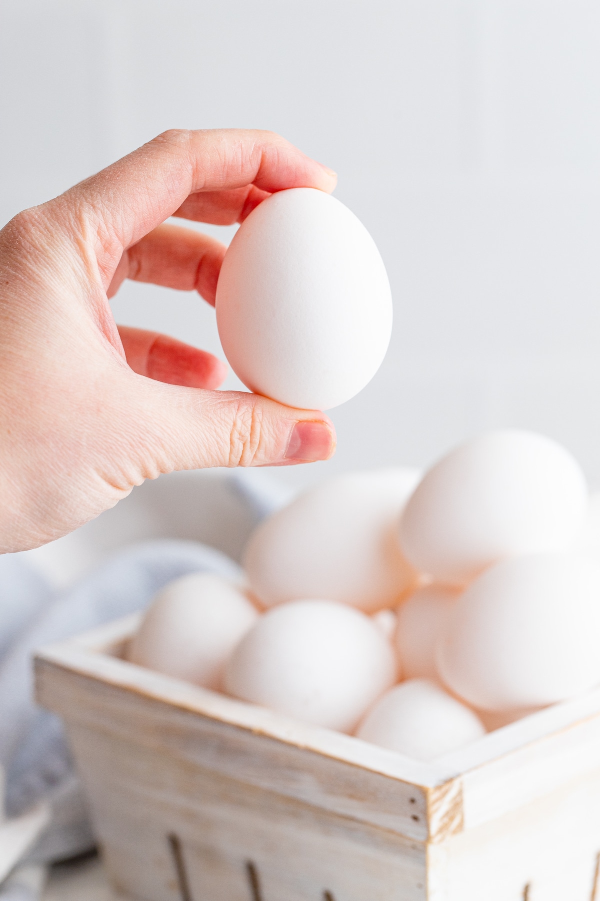 Hand holding up one egg with more in a basket below it
