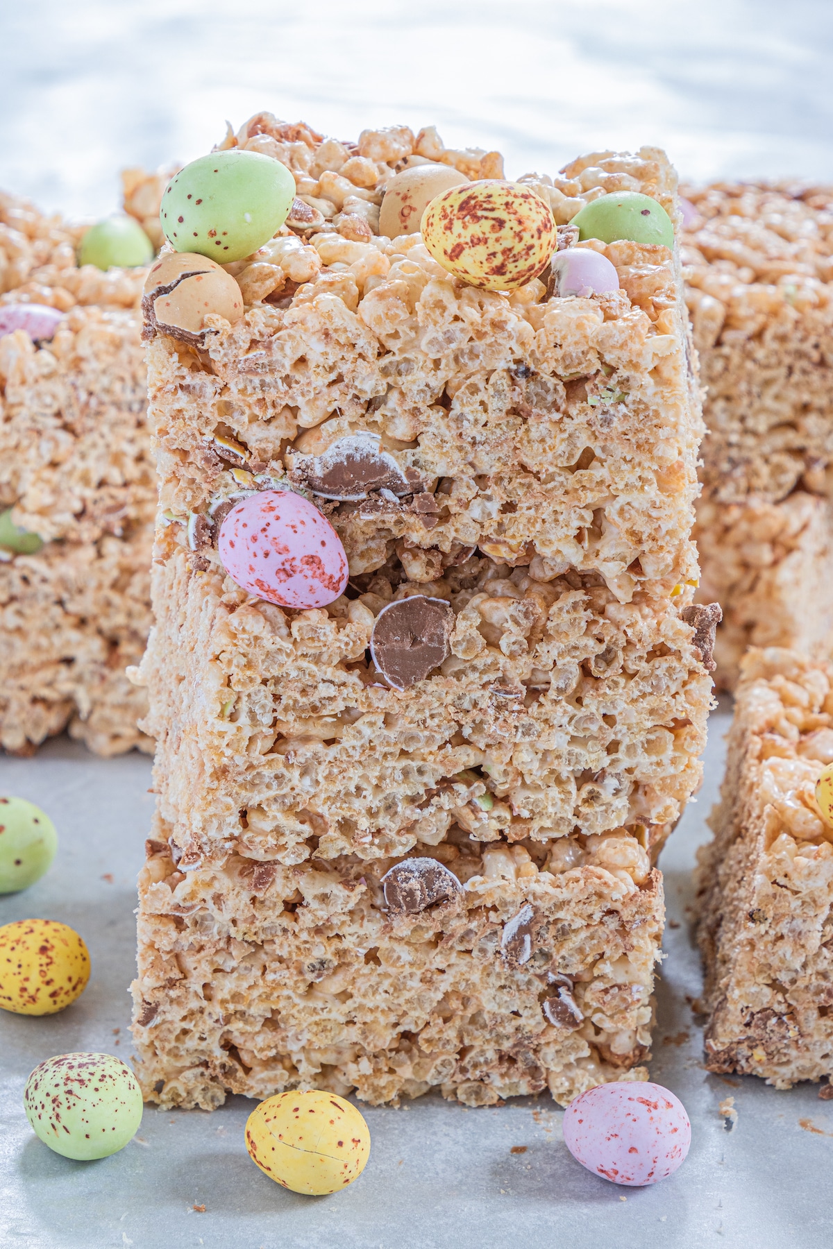 Three Easter rice krispie treats stacked on eachother with more chocolate egg candies around them