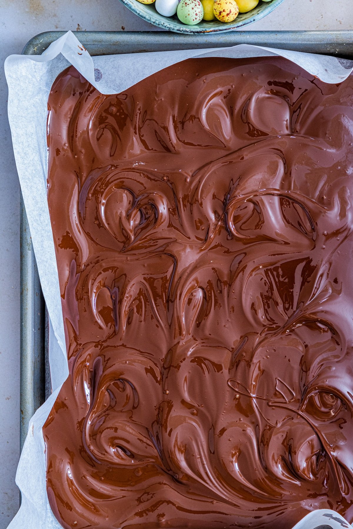 Overhead shot of melted chocolate spread out on a parchment lined baking sheet