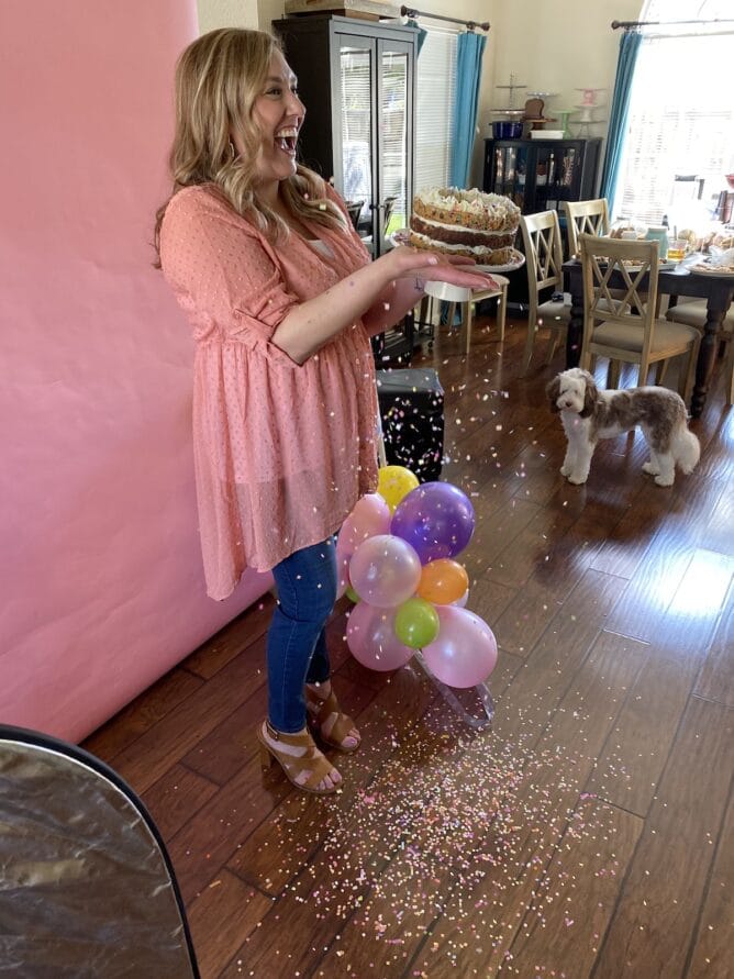 woman in pink shirt with pink background holiding cake and throwing confetti