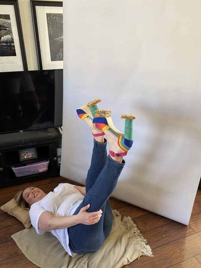 woman laying on ground with feet in the air and cookies balanced on rainbow shoes