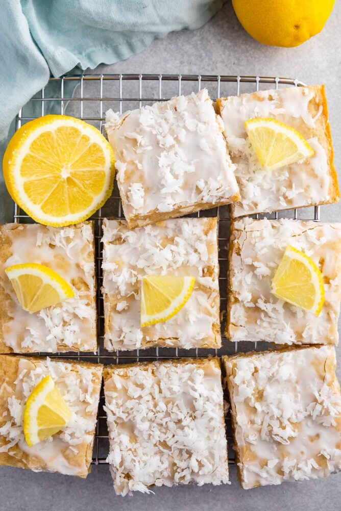 Overhead shot of lemon coconut blondie squares on a wire cooling rack with lemon wedges on top