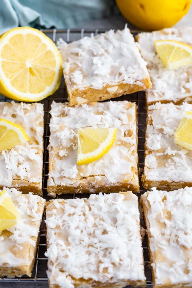 Overhead shot of lemon coconut blondie squares on a wire cooling rack with lemon wedges on top