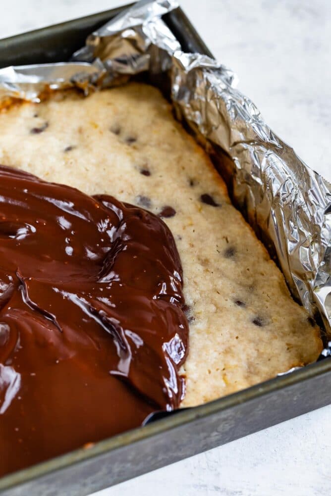 Easy chocolate chip banana bars in baking pan with chocolate ganache being spread on top