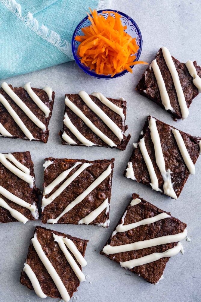 Overhead shot of carrot cake brownies cut into squares next to a cup of shredded carrots