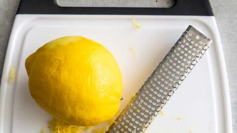 Overhead shot of lemon being zested over a cutting board with blog title on top of image