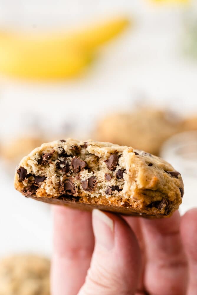 Hand holding a banana chocolate chip cookie that's cut in half